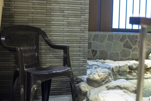 A plastic chair against a brick wall with a stone wall and rocks in the foreground.