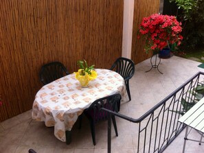 A round table with a patterned tablecloth, surrounded by four chairs, set on a tiled patio with a bamboo fence in the background. - La Casina (Massa)