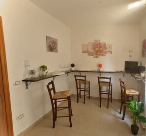 A compact kitchen with a bar area, four wooden chairs, a potted plant, and wall art. - B&B Sogni d'Oro (Reggio Calabria)