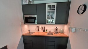 Eine kleine Küche mit dunklen Schränken, einer Mikrowelle, einem Spülbecken und einer Kaffeemaschine.