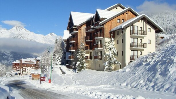 Ein mehrstöckiges Hotel mit Balkonen, gelegen an einem verschneiten Hang mit Bergen im Hintergrund.