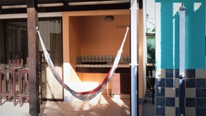 Una cadira espanyola penjada entre bigues de fusta en una habitació il·luminada pel sol, amb un paviment i una paret de rajoles, i una finestra amb cortines.