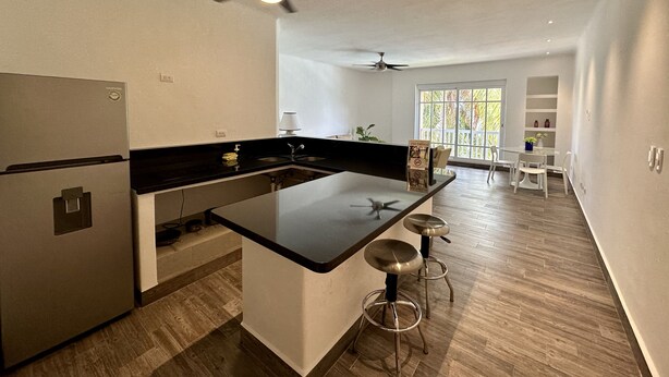 Una cocina moderna con una isla central, dos taburetes de bar, un refrigerador y un ventilador de techo.
