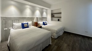 Una habitación de hotel con dos camas, ventilador de techo, luces empotradas y estante integrado.