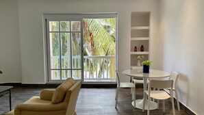 Un moderno salón con un sofá, una mesa de vidrio y sillas. Se ve un ventanal con vistas a palmeras.