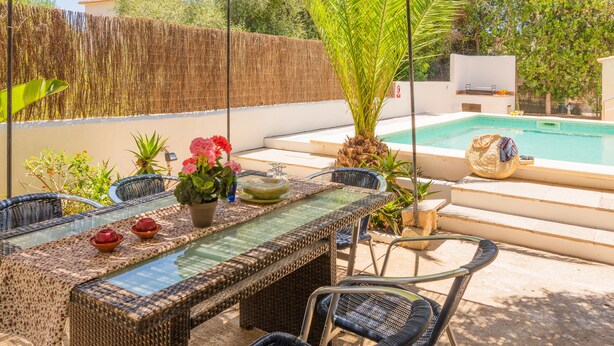 Un espace aménagé au bord de la piscine, avec une table à manger, des chaises et une piscine.