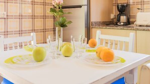 Une cuisine avec une table blanche mise pour deux personnes, agrémentée d’un vase avec une fleur, de deux pommes et de deux oranges.