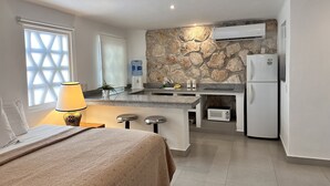A compact hotel room with a kitchenette, a bed with a patterned bedspread, a lamp, and a stone accent wall. - COZY STUDIO WITH FULL KITCHEN ★ AMAZING LOCATION (Cancún)