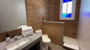 A modern bathroom with a wooden wall, a sink with a mirror, a toilet, and a shower area. - COZY STUDIO WITH FULL KITCHEN ★ AMAZING LOCATION (Cancún)
