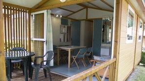 Een houten terras met een tafel, stoelen, een magnetron en een raam met gordijnen.
