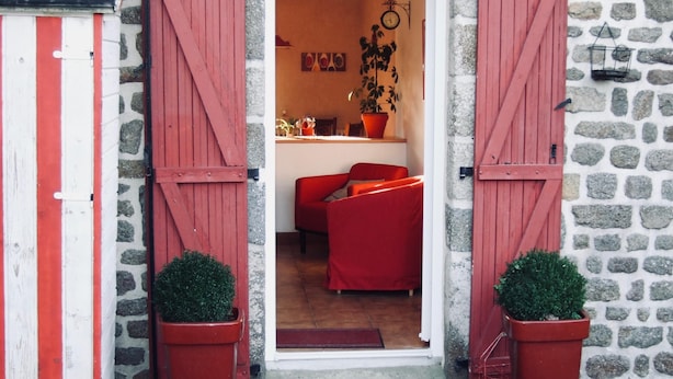 Ein Gebäude aus Stein mit roten Fensterläden, einem roten Stuhl und einem Blumentopf darin.