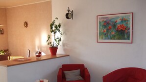 Ein Wohnzimmer mit einem roten Sofa, einem kleinen weißen Tisch, einer Topfpflanze und einem Gemälde an der Wand.