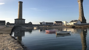 Escena costera con dos torres destacadas, una masa de agua tranquila con barcos y varios edificios a lo largo de la orilla.