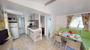 Een kleine keuken met een magnetron, fornuis en wastafel, een eethoek met een tafel en stoelen, en uitzicht op de omgeving door een raam.