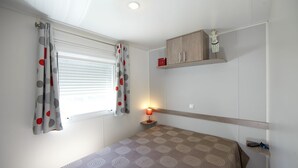Een slaapkamer met een bed, nachtkastje, lamp, plankje met een klein object en een raam met gordijnen.