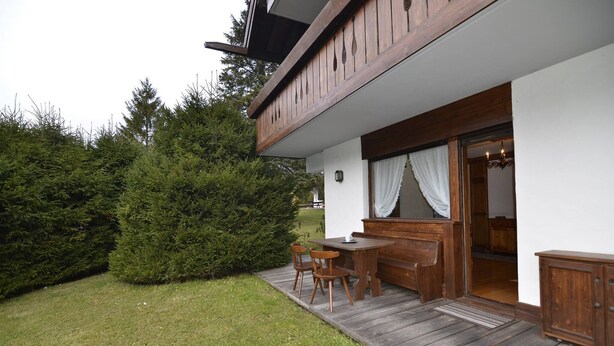 A wooden deck with a table and chairs, a wooden bench, and a door leading inside. - Punta Nera Apartment: WI-FI and garden. (Cortina d´Ampezzo)