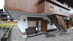 A two-story wooden house with a stone-paved entrance and a wooden staircase leading to the upper floor. - Punta Nera Apartment: WI-FI and garden. (Cortina d´Ampezzo)