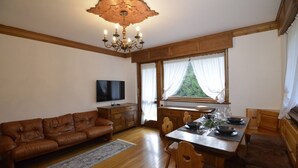 A cozy living room with a brown leather sofa, wooden dining table, and a chandelier. - Punta Nera Apartment: WI-FI and garden. (Cortina d´Ampezzo)
