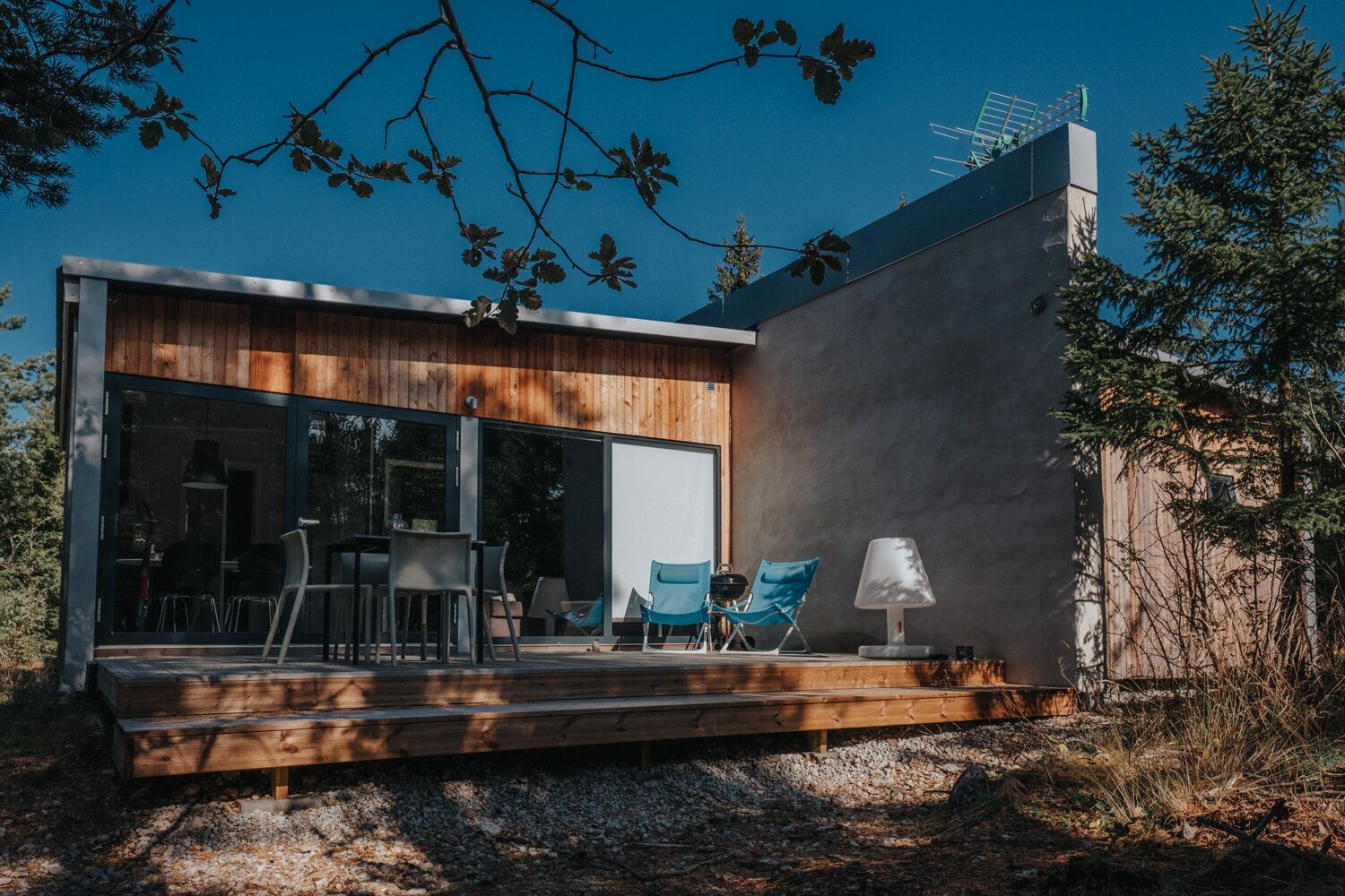 A modern house with a wooden deck, outdoor seating, and a large sliding glass door.