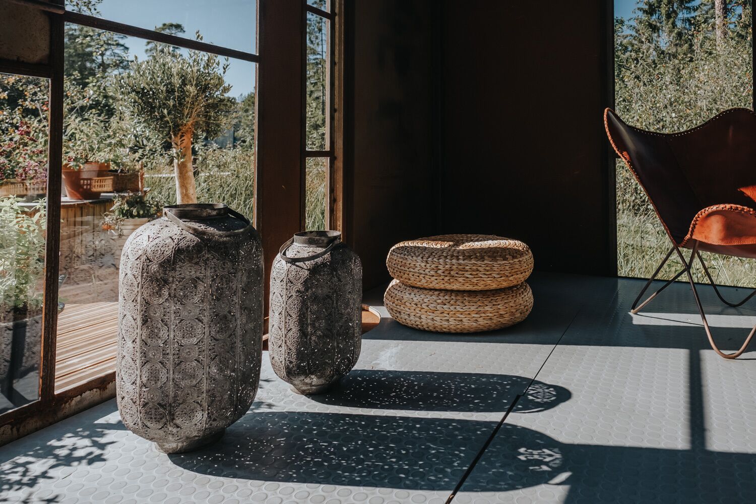 Un interior moderno con amplios ventanales, un rincón de estar con cestas tejidas y una maceta de piedra rústica.