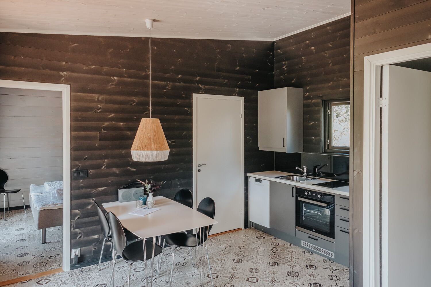 Une cuisine compacte dotée d’un plan de travail blanc, d’un four encastré et d’un four à micro-ondes. On y trouve également un coin repas avec une table blanche et des chaises noires.
