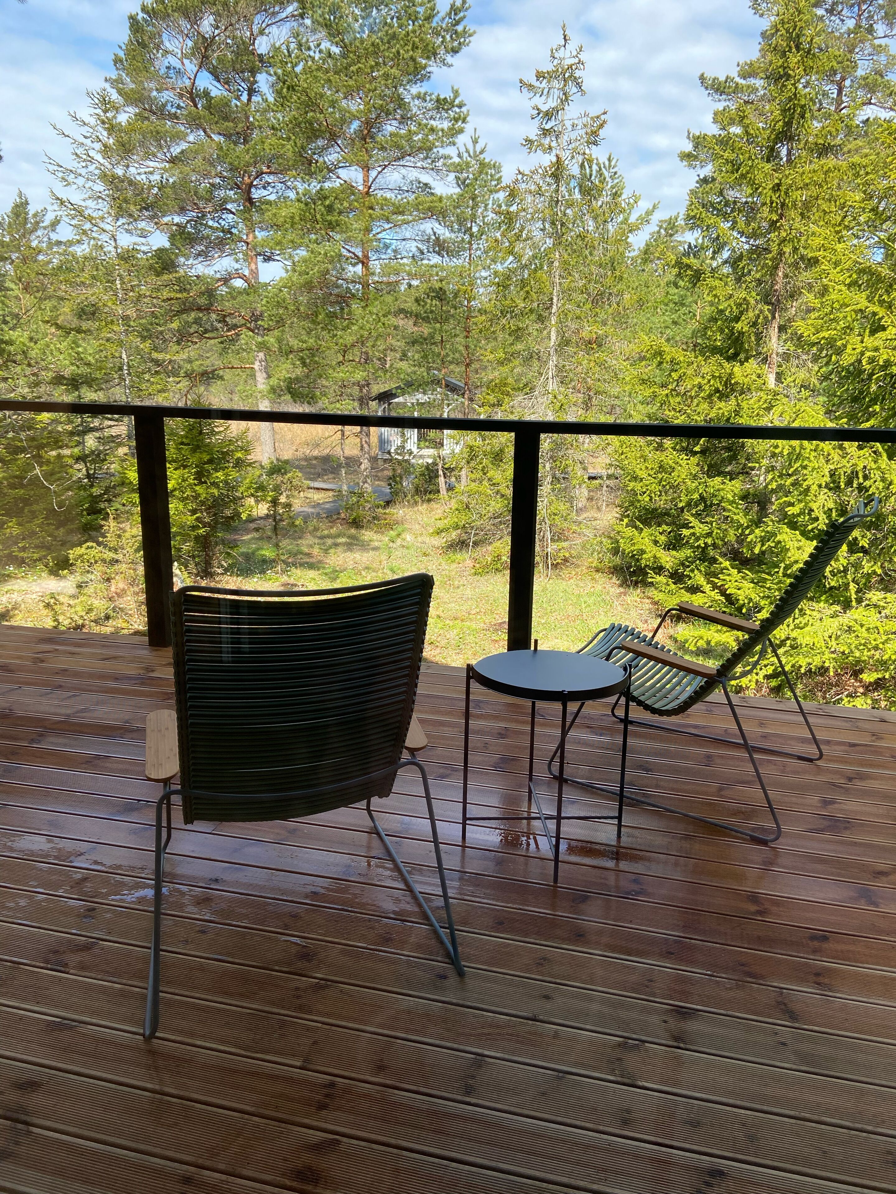 A wooden deck with a metal railing, a black chair, and a small table.
