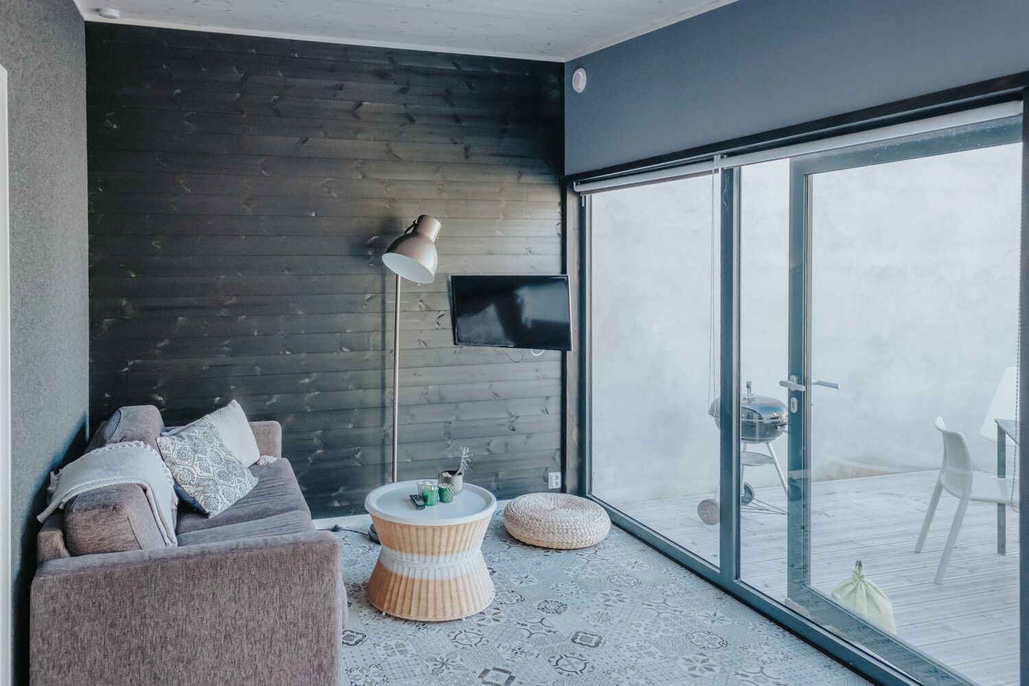 A modern living room with a dark wooden wall, a sofa, a round coffee table, and a large glass door leading to an outdoor area.