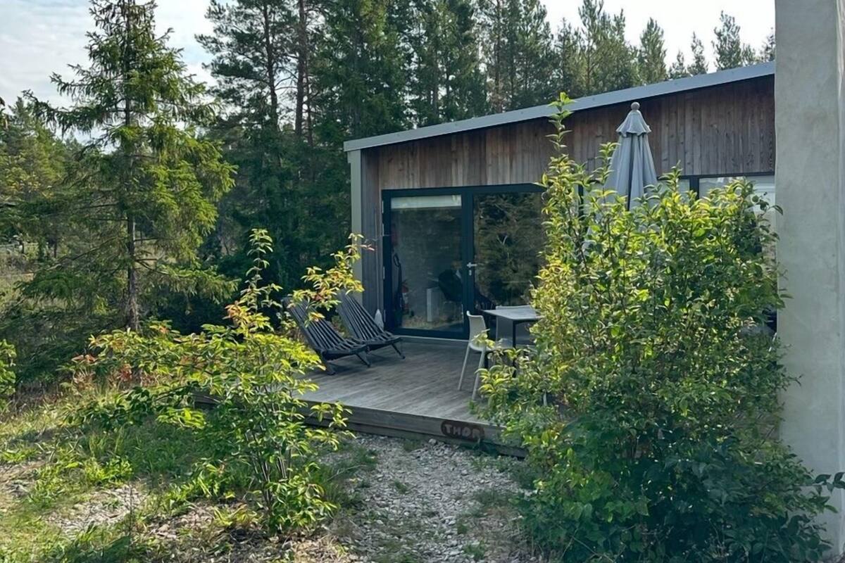 A modern house with a deck, a glass door leading to a patio, and a view of a forested area.
