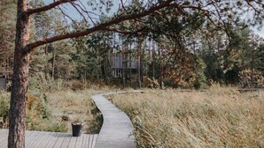 A wooden boardwalk leading through a forested area with a cabin in the background. - Mavens Kustnära Stugor (Lärbro)
