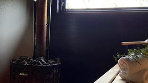 A wood-burning stove with visible flames, a bench, and a window with daylight. - Mavens Kustnära Stugor (Lärbro)