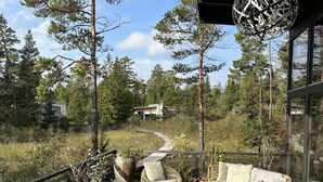 A wooden deck with wicker furniture, potted plants, and a hanging light fixture. - Mavens Kustnära Stugor (Lärbro)