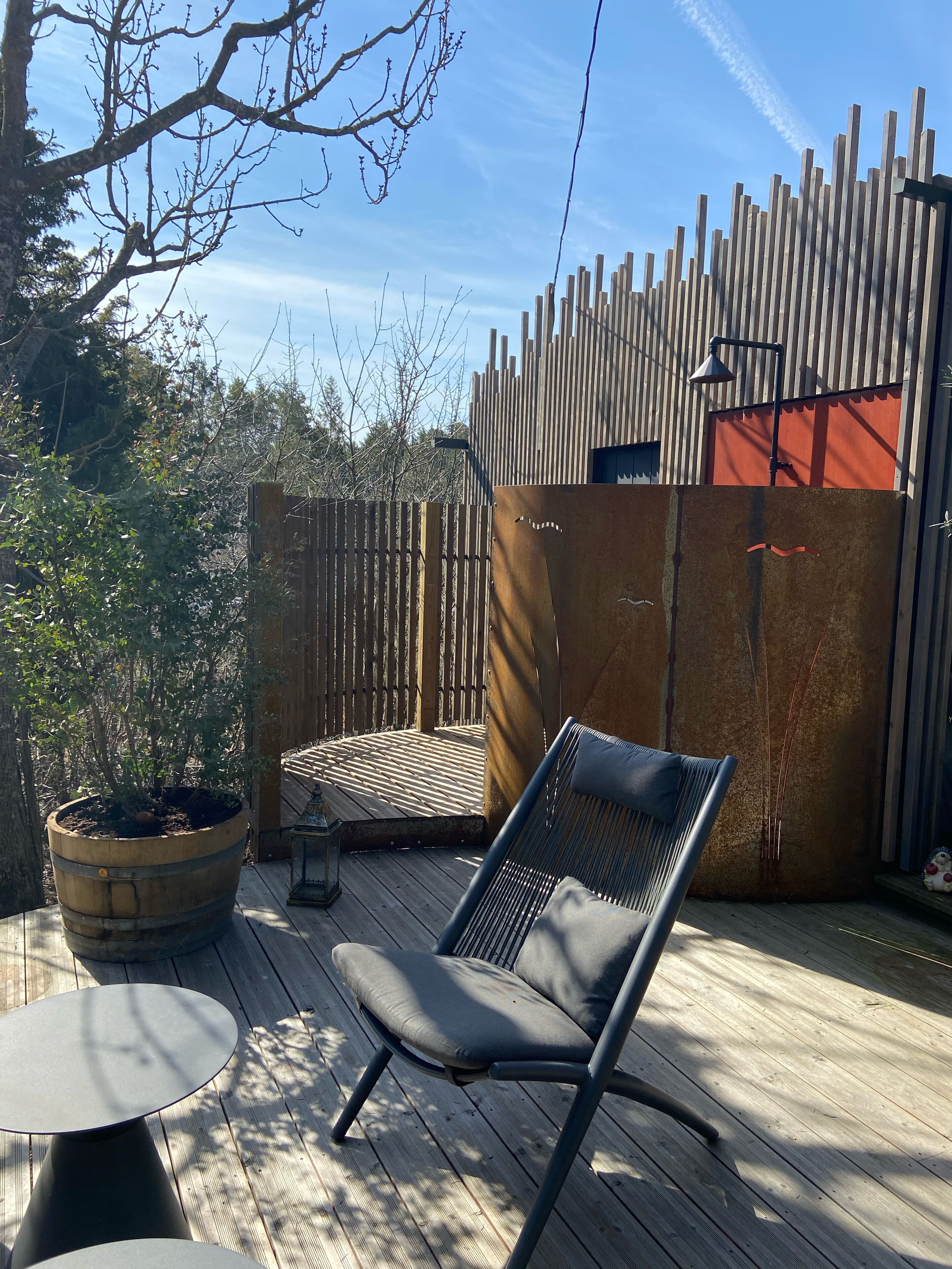 A wooden deck with a metal chair and a table, surrounded by a wooden fence and a potted plant.