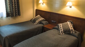 Una habitación con dos camas individuales, cada una con un cojín estampado y un cabecero de madera. Hay dos lámparas fijadas a la pared que proporcionan luz.