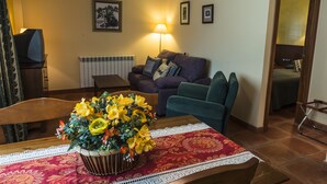 Una sala de estar con un sofá, sillones, una mesa de centro con un centro de flores, una lámpara y un radiador.