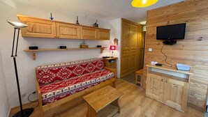 A cozy living room with a wooden bench, a small table, and a TV mounted on a wooden wall. - Cozy 2-room apartment, 5 people, Les Saisies (Les Saisies)