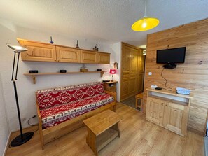 A cozy living room with a wooden bench, a small table, and a TV mounted on a wooden wall. - Cozy 2-room apartment, 5 people, Les Saisies (Les Saisies)