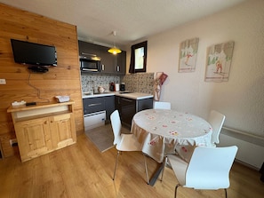 A compact kitchen with modern appliances, a dining area with a round table and chairs, and a wall-mounted TV.