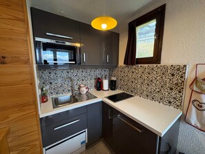Cocina compacta con microondas, lavabo y una ventana pequeña.