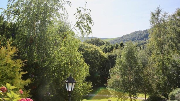 A lush garden with a pathway, a lamppost, and a view of a valley. - Heather House (Glendalough)