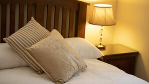 A neatly made bed with two pillows and a wooden headboard. There is a bedside table with a lamp and a small drawer. - Heather House (Glendalough)