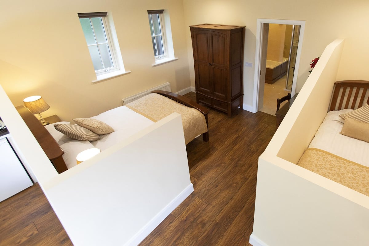 A bedroom with two beds, a wardrobe, and a bathroom visible through an open door.