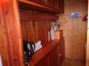 Interior de una cabaña de madera con una zona de cocina, que incluye una cafetera, un tostador y un juego de cuchillos en la encimera.