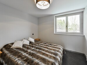 Ein Schlafzimmer mit einem großen Bett, einem Fenster mit Blick auf Bäume und einer Deckenleuchte.