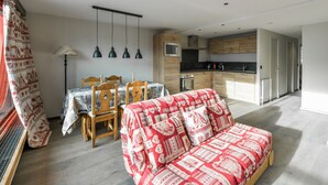 A modern living room with a sofa, dining table, chairs, and a kitchen area with wooden cabinets and appliances. - Renovated 2BR apartment at ski slopes with parking - Courchevel 1850 (Courchevel 1850)
