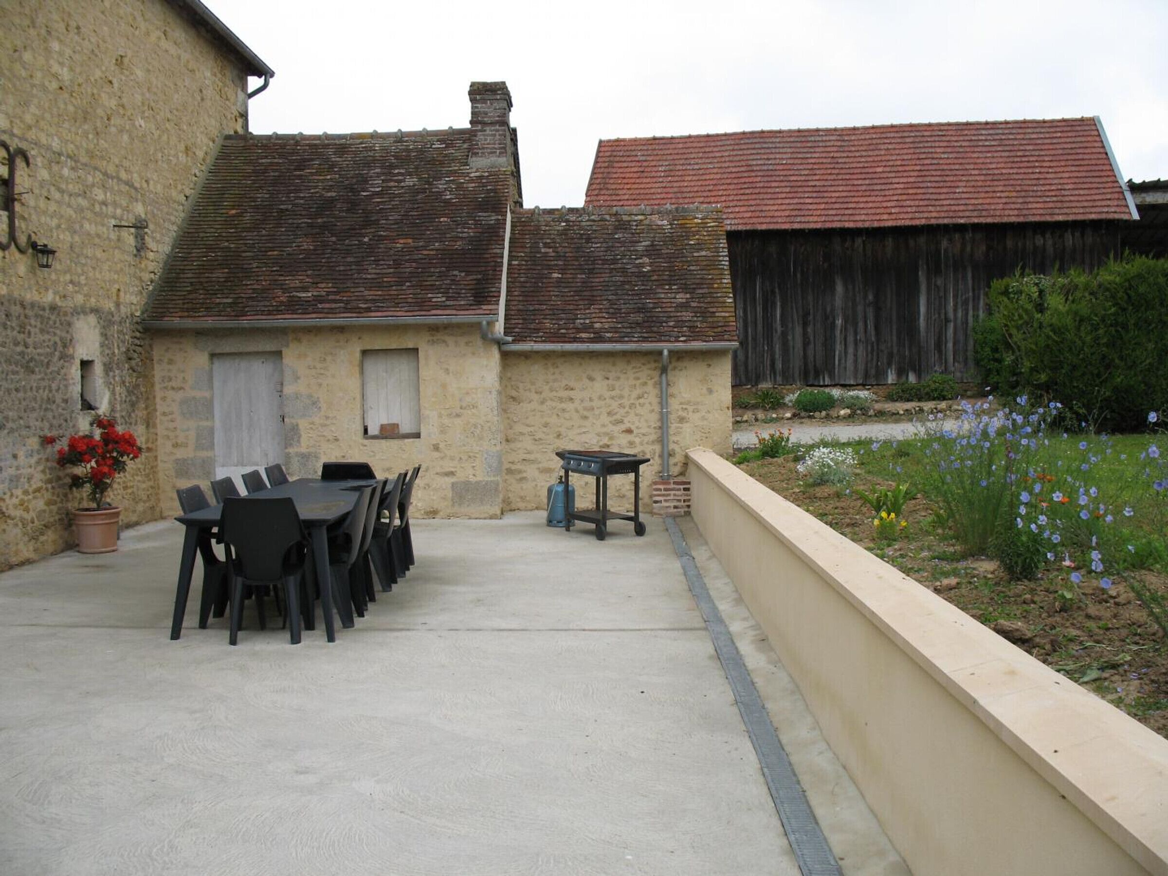 A courtyard with a table and chairs, a potted plant, and a garden with flowers.