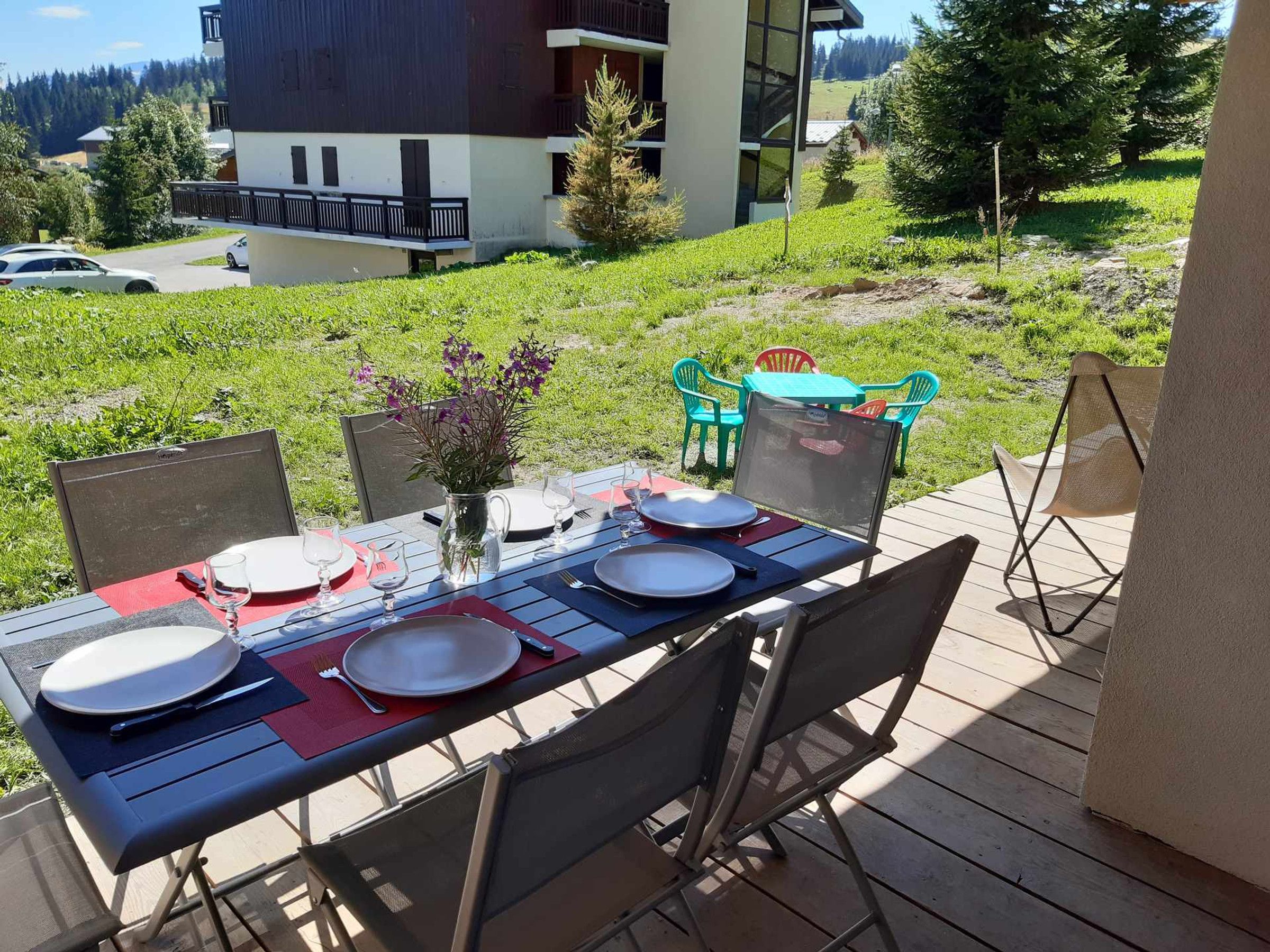 An outdoor dining area with a table set for four, surrounded by chairs, on a wooden deck.