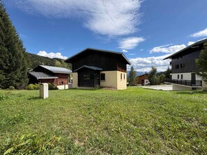 A cluster of wooden houses with a grassy foreground and a mountainous backdrop.