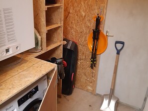 A room with a washing machine, a guitar case, and a shovel on the floor.