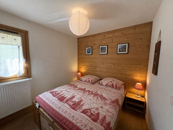 A bedroom with a wooden headboard, a bed with a patterned bedspread, two bedside lamps, and a window with curtains.
