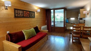 A wooden cabin with a sofa, a dining table, and a kitchen area. - Cozy studio with west balcony, WIFI, covered parking (Brides-les-Bains)
